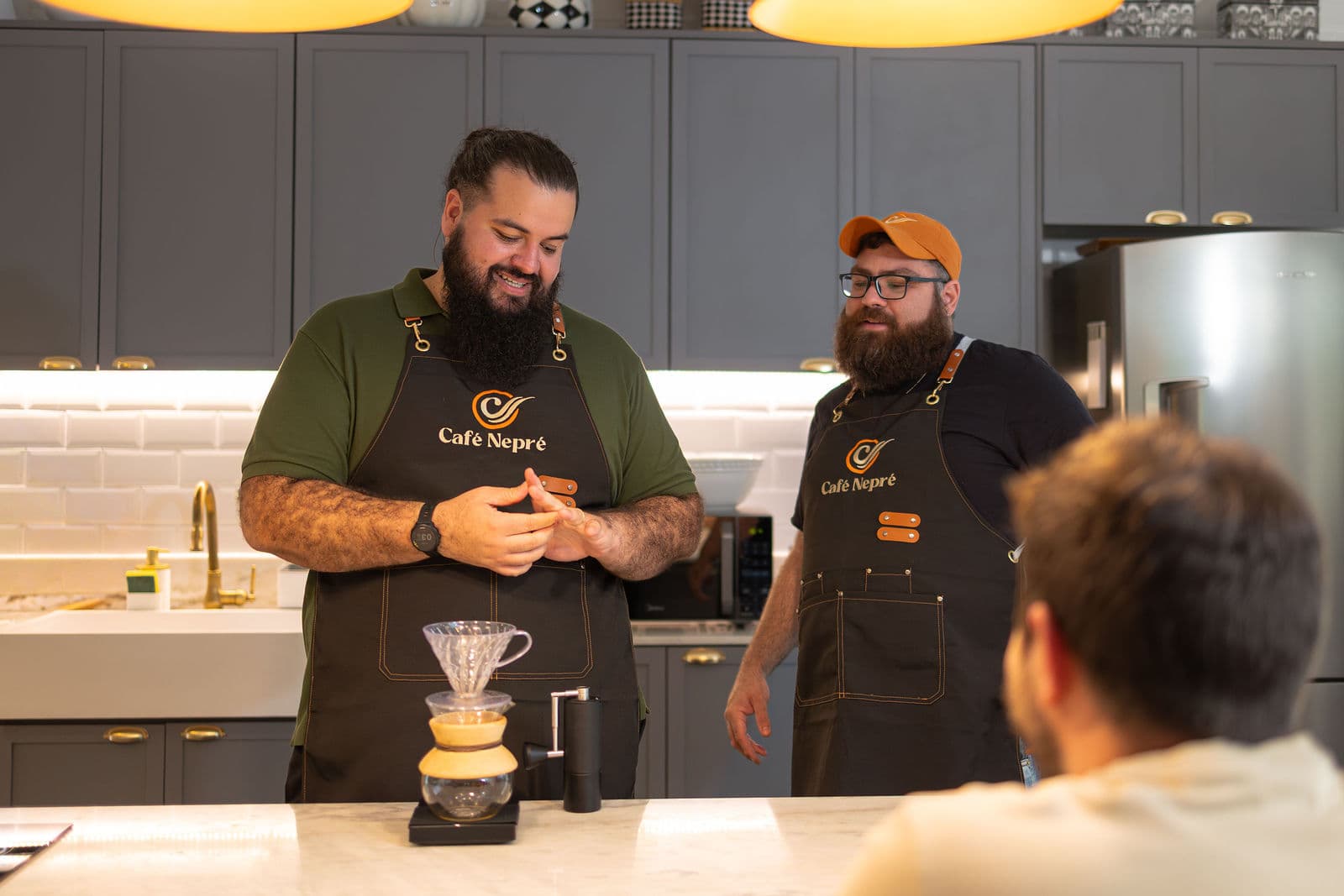 Dois fundadores do Café Nepré, de avental da marca, preparando um coado na bancada